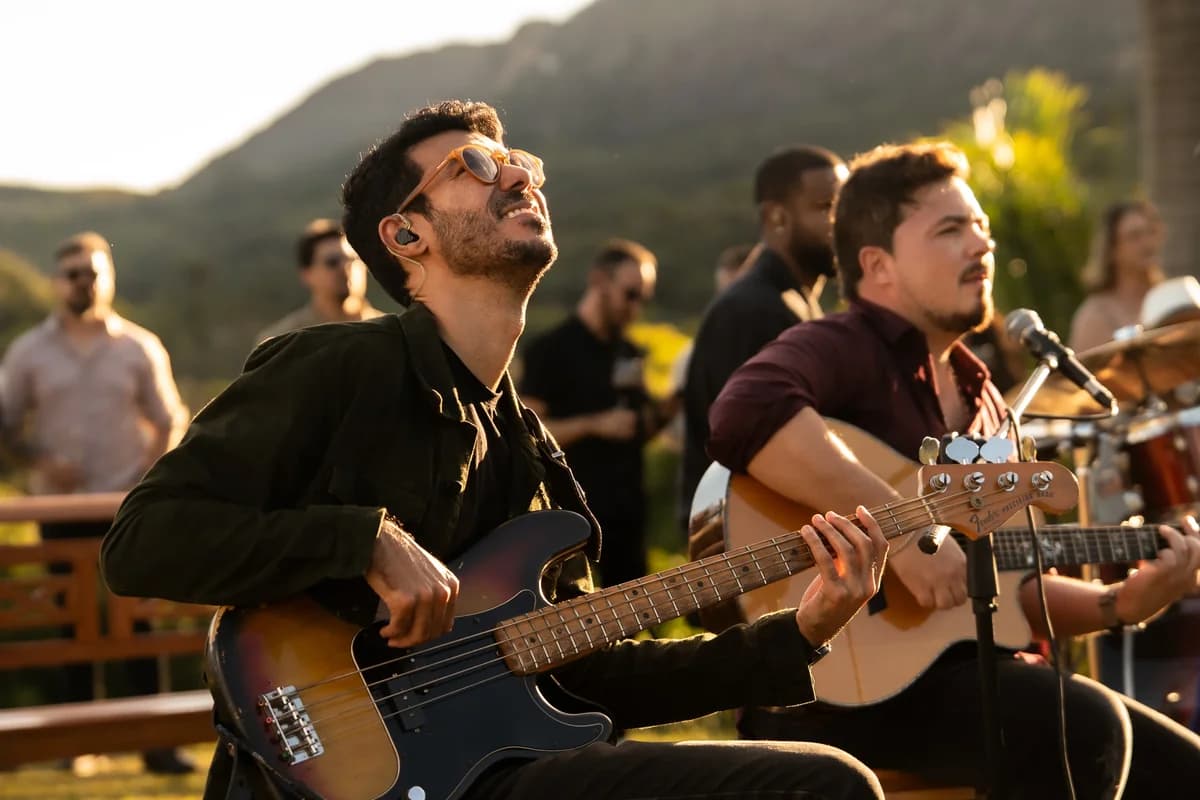 Baixista e violonista tocando lado a lado no contraluz dourado do entardecer